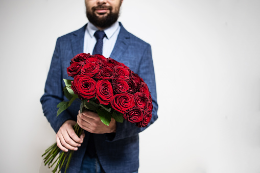 Close up of a luxurious bouquet in the hands of a man in a suit on a gray background. Concept: holiday, flower delivery, postcard, mothers day, womens, proposal, date, macho, red roses,