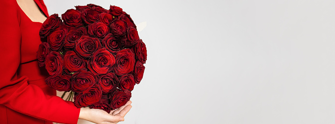 Portrait of woman holding big bouquet of red roses with big red bow in front of her face isolated on white background