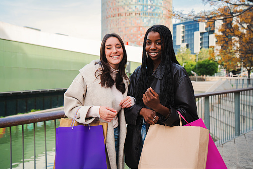 happy young women friends with shopping bags smiling and looking at camera after purchase some clothes retails at the mall in the sale week. High quality photo