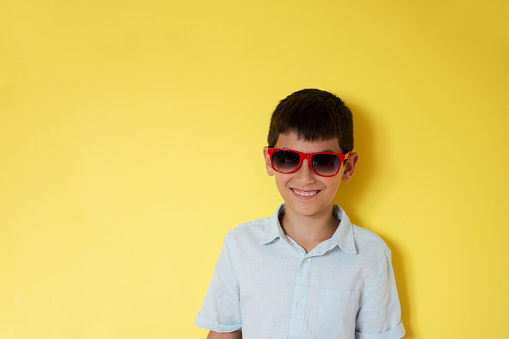 A boy in black sunglasses with his arms crossed and his mouth open funny poses on a yellow background