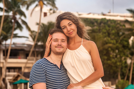 Portrait lovely couple hugging enjoying honeymoon summer at tropic background, looking at camera. Happy couple in love cuddling on tropical coast. Family travel vacation concept. Copy ad text space