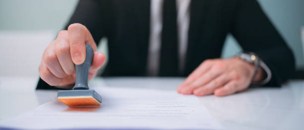 istock Businessman hand stamping an approved stamp on a text document at a table with a contract form paper in the background. 1468256595