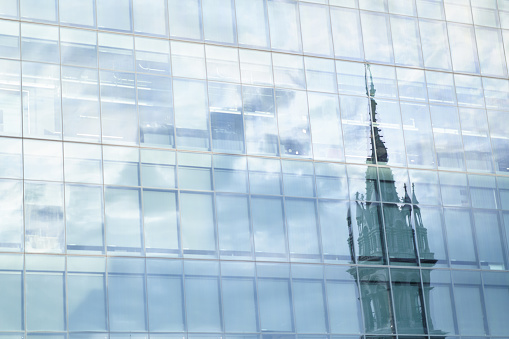The bell tower of a church reflected on the facade of a skyscraper building in the downtown district of Montreal