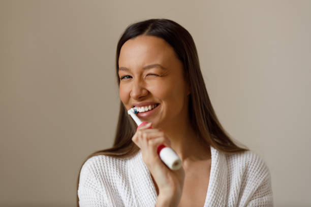 Portrait of young woman engaged in everyday procedures after shower. Brushing your teeth with electric toothbrush. Snow-white smile. Care, beauty and health. stock photo