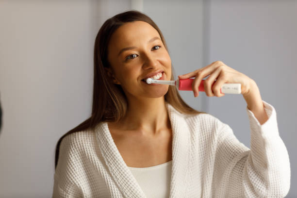 Portrait of young woman engaged in everyday procedures after shower. Brushing your teeth with electric toothbrush. Snow-white smile. Care, beauty and health. stock photo