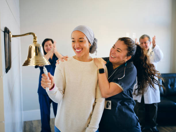 Adult Woman Chemotherapy Patient Finishing Treatment with a Ceremonial Bell Ring An adult woman chemotherapy patient in a treatment office, celebrating the completion of her treatment with a ceremonial bell ring. Actor portrayal. cancer treatment stock pictures, royalty-free photos & images
