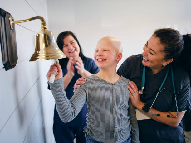 Child Chemotherapy Patient Finishing Treatment with a Ceremonial Bell Ring A young child girl chemotherapy patient in a treatment office, celebrating the completion of her treatment with a ceremonial bell ring. Actor portrayal. real symbol stock pictures, royalty-free photos & images