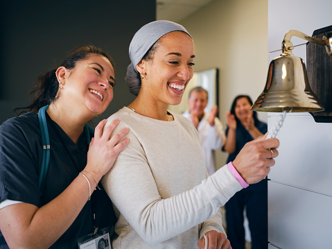 An adult woman chemotherapy patient in a treatment office, celebrating the completion of her treatment with a ceremonial bell ring. Actor portrayal.