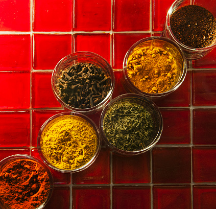 Samples of multi-color spices in round glasses on square red tiles