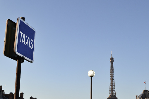 Paris skyline at morning with Eiffel Tower and urban elements such as: a taxi sign, chimneys, street light.