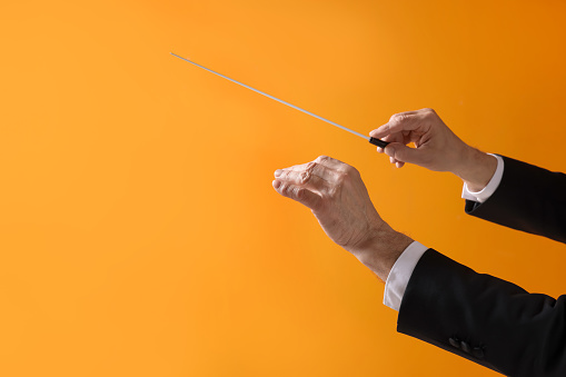 Professional conductor with baton on orange background, closeup. Space for text