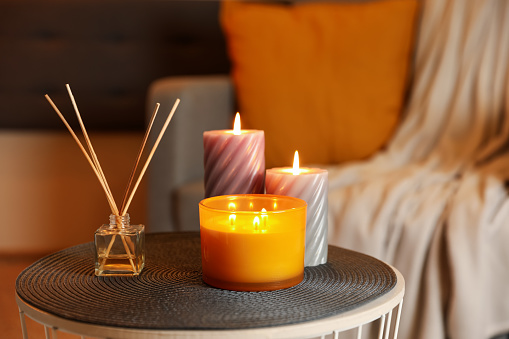 Burning candles and reed air freshener on table indoors. Cosy atmosphere