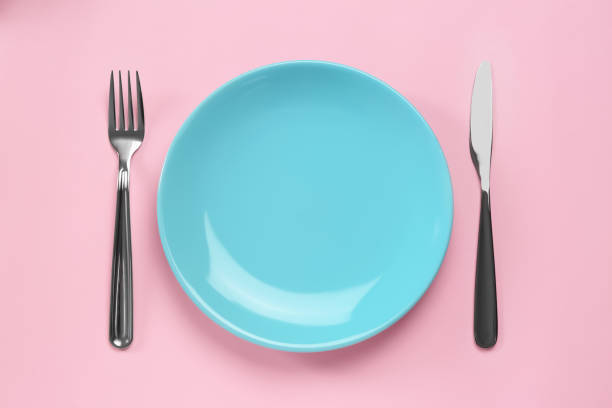 istock Clean plate and shiny silver cutlery on pink background, flat lay 1468277650