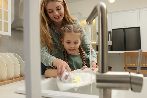 Mother and daughter washing plate above sink in kitchen, view from outside