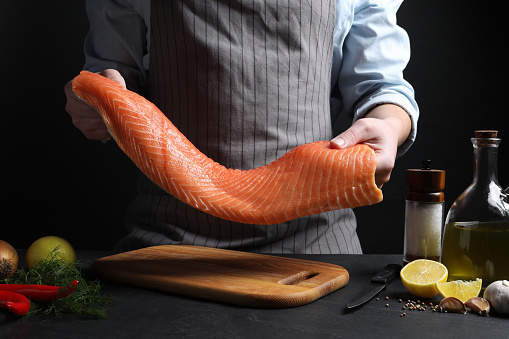 Man with raw salmon fillet at black table, closeup