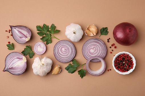 Fresh red onions, garlic, parsley and spices on beige background, flat lay