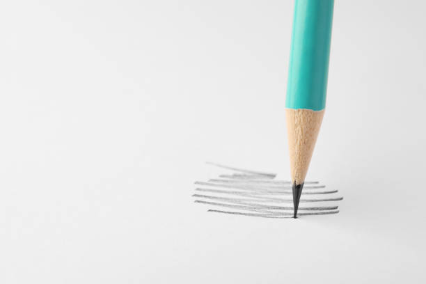 High resolution shot of a black carbon graphite / sharp tip or solid pigment core of a pencil with drawing line on textured white paper. Pencil shows wood fiber that prevents the nib from being broken