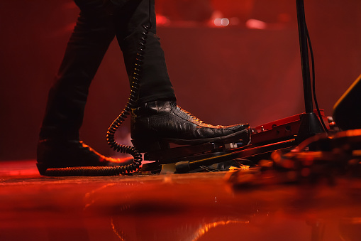 Rocker wearing black cowboy shoes using pedal while playing on a guitar in red stage lights
