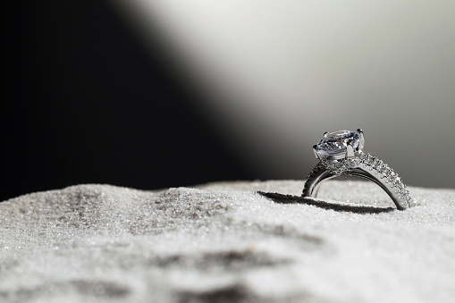 Luxury jewelry. Stylish presentation of ring in sand against dark background, closeup. Space for text