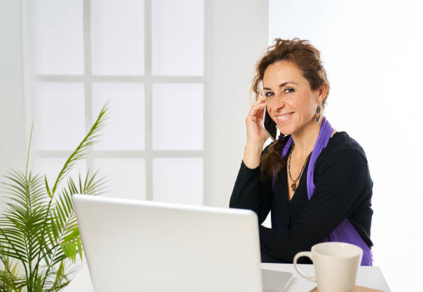 Elegant blonde mid adult businesswoman at white background, uses mobile phone, notebook, copyspace.