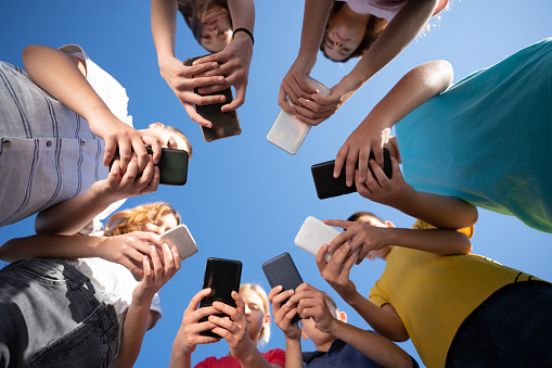 Low angle view of group of teenage children standing in the circle and using mobile phones