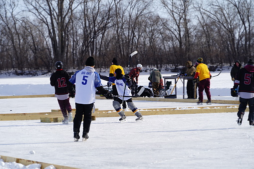 Oshkosh, Wisconsin USA - February 4th, 2023: Group of male friends playing hockey together on a frozen lake during the Winter season.