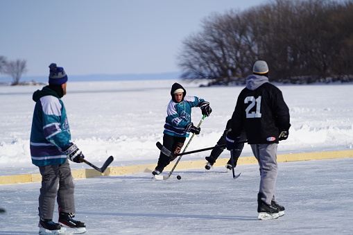 Oshkosh, Wisconsin USA - February 4th, 2023: Group of male friends playing hockey together on a frozen lake during the Winter season.