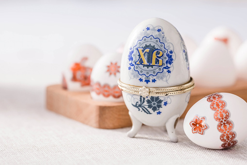 A large egg-box with the inscription XB and Easter eggs on a linen tablecloth on the table. The concept of the Bright Easter holiday.