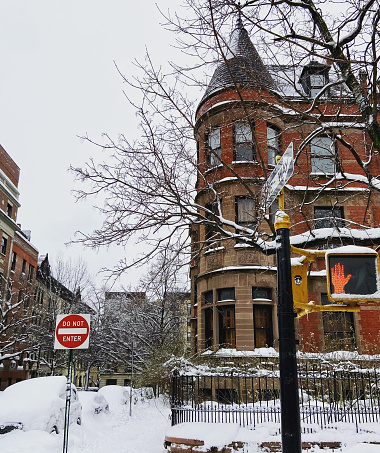 Snow covers the turret of a historic townhouse on a corner of Convent Avenue in Harlem, New York City, with a street light and signs in front