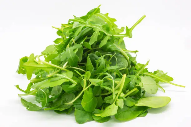 A close up of a handful of salad leaves, with a white background behind