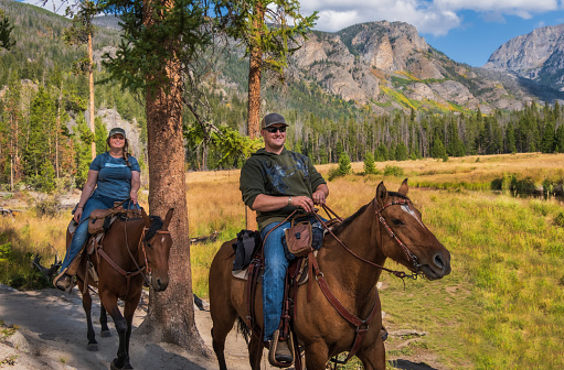 Smiling young man and woman riding horses in the forest of Rocky Mountains, Colorado.