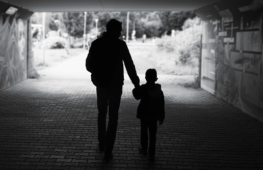 Silhouette of father walking with his son down a city street.