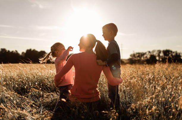 Mère et ses deux enfants garçon et fille se relaxant dans le champ d’herbe de la nature en regardant le coucher du soleil. - Photo