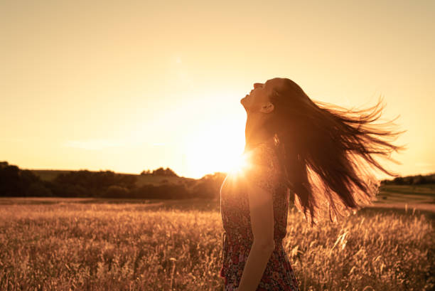 Giovane donna che alza lo sguardo sentendosi felice in natura - foto stock