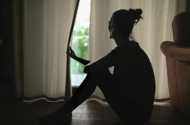 joven triste mirando por la ventana - abrazar las rodillas fotografías e imágenes de stock