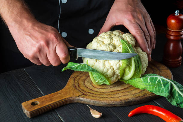 chef profissional corta couve-flor na cozinha de um restaurante antes de cozinhar. a ideia de uma dieta deliciosa para o café da manhã ou jantar - hotel commercial kitchen organic salad - fotografias e filmes do acervo