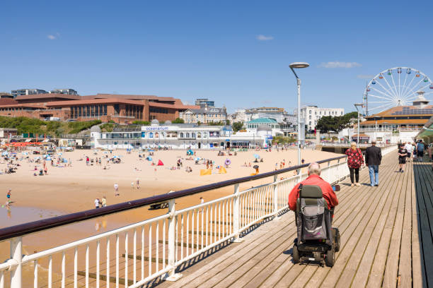 Bournemouth, UK - July 08, 2022. Elderly man on a mobility scooter on the promenade of Bournemouth Pier, Dorset, UK. Old age and disability