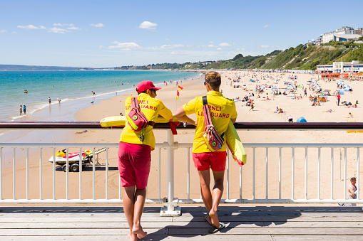 Bournemouth, UK - July 08, 2022. Two RNLI lifeguards in uniform watching Bournemouth beach from the pier during summer.