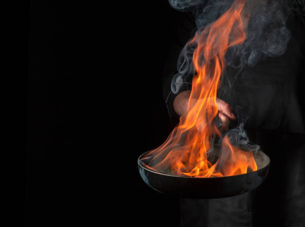 istock Professional chef cooking food in pan with fire flame on black background. Restaurant and hotel service concept. Free advertising space 1468300055