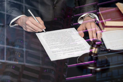 The concept of legal support in the signing of documents. Lawyer signs a document on a blurred background at the table.