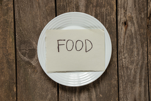 white empty clean plate with a sheet of paper on which food is written stands on a wooden table, plate on the table