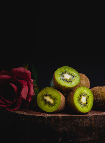 close-up of natural and organic kiwis, on piece of wood, with black background, and red flower, space to copy.