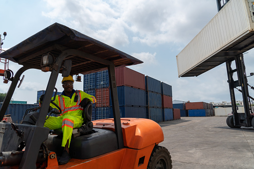 African american man driving forklift in shipyard . Logistics supply chain management and international goods export concept .