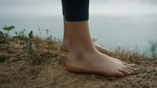 Bare legs unknown woman going on dry grass sandy hill close up. Unrecognizable girl stop at hilltop enjoying calm sea view cloudy morning. Young lady feet walking seacoast outdoors. Nature concept.