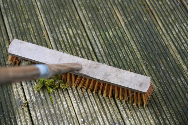 Outdoor broom with plastic bristles scrubbing a weathered wooden deck to remove algae and moss, spring cleaning in garden and yard, copy space, selected focus stock photo