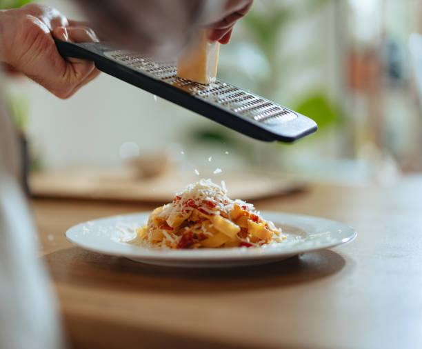 foto ravvicinata delle mani dell'uomo che grattugia il formaggio nella pasta con verdure fresche - grater foto e immagini stock