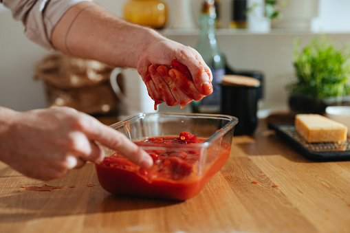 An anonymous chef making a healthy meal with tomato sauce in a bowl at the kitchen table.