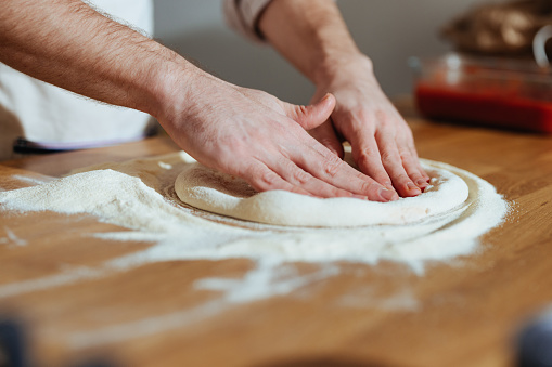 High angle view of an anonymous chef making homemade pizza dough on a kitchen table.