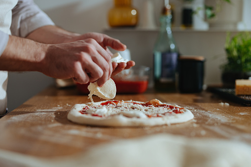 An anonymous chef in apron making homemade pizza on the kitchen table.