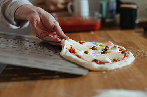An anonymous chef in apron making homemade pizza on the kitchen table.
